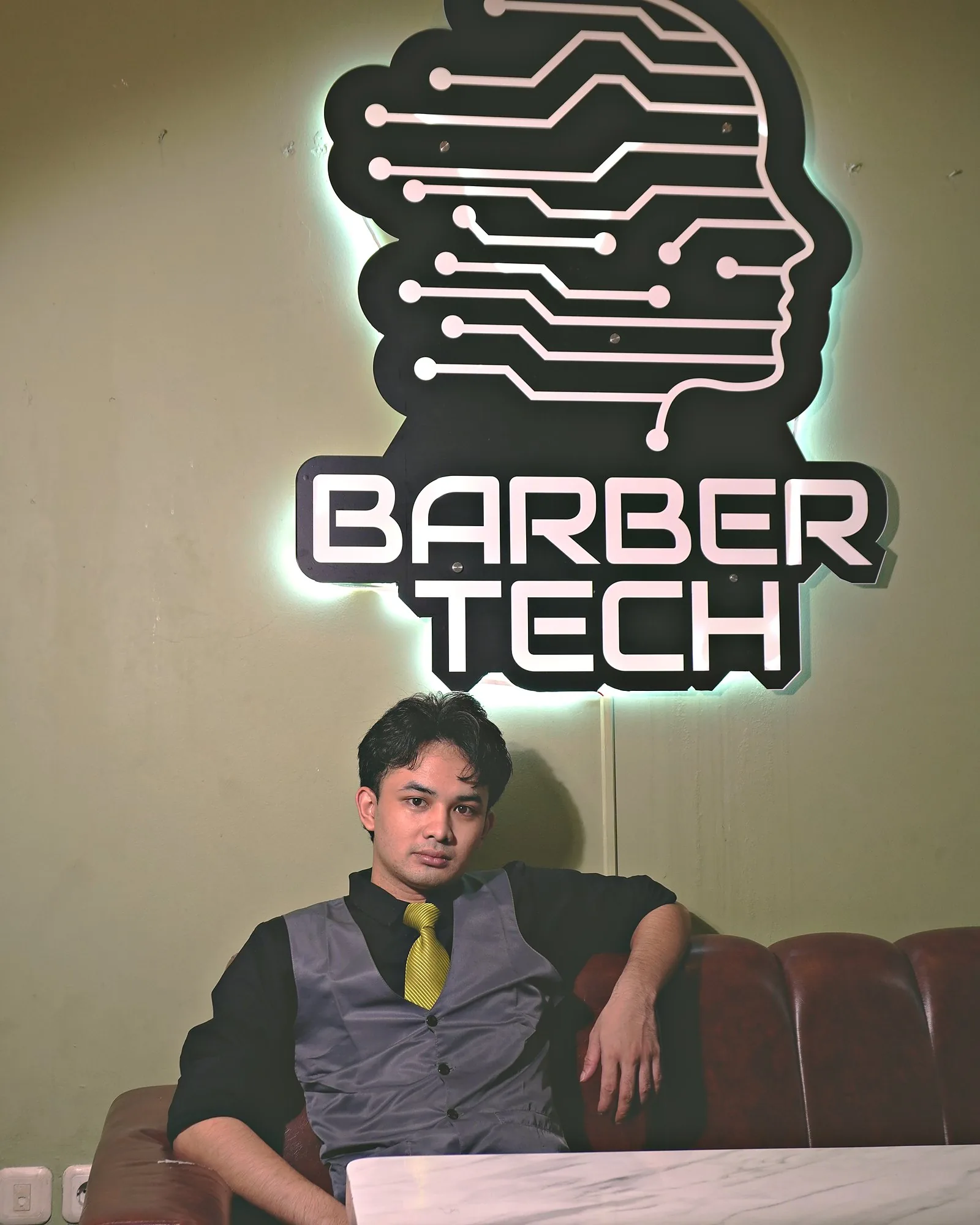 Pelanggan duduk santai di depan papan nama Barbertech yang menyala