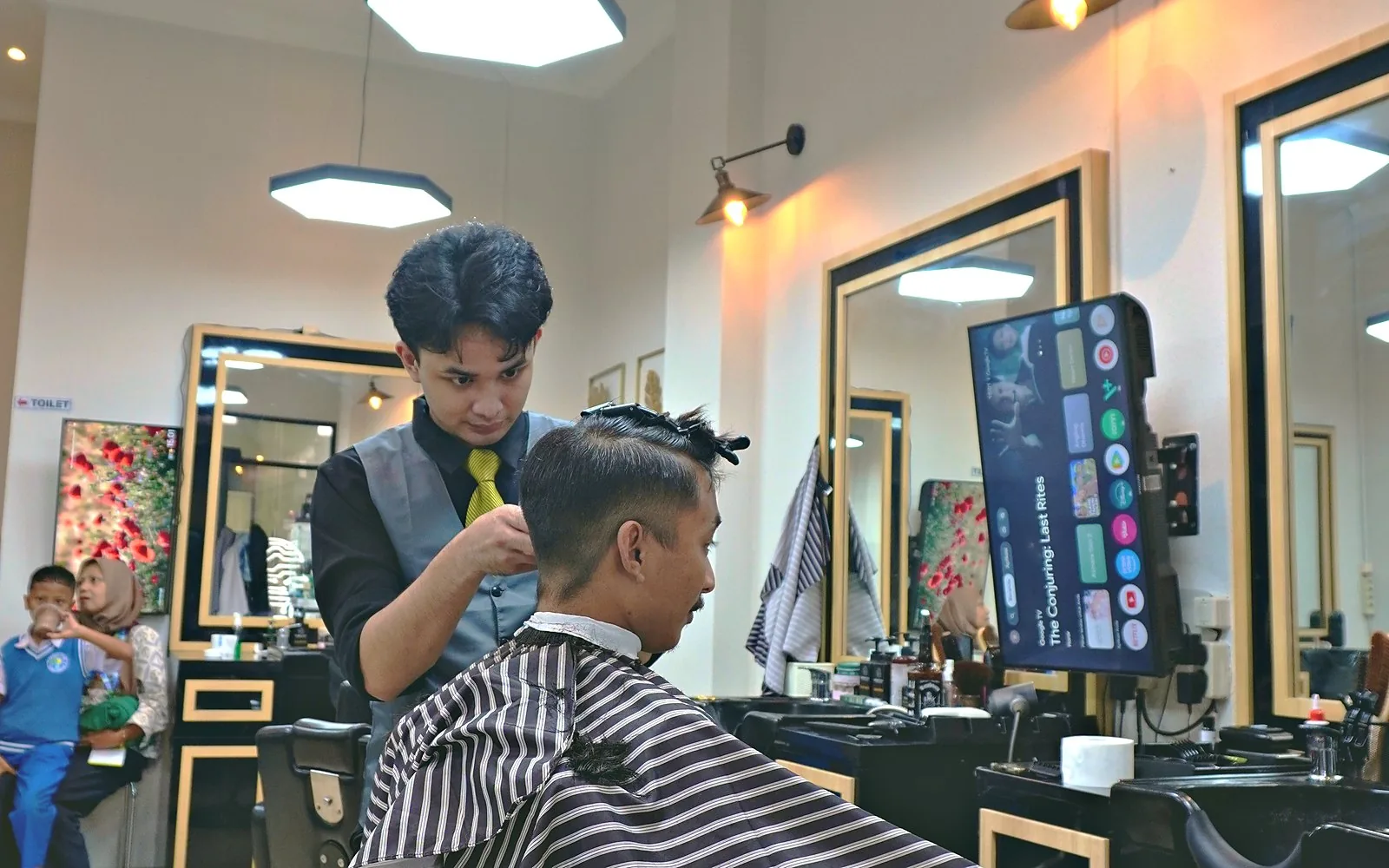 Capster merapikan bagian samping dengan clipper